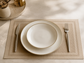 Square light brown placemat with white gold-rimmed plates on dark dining table