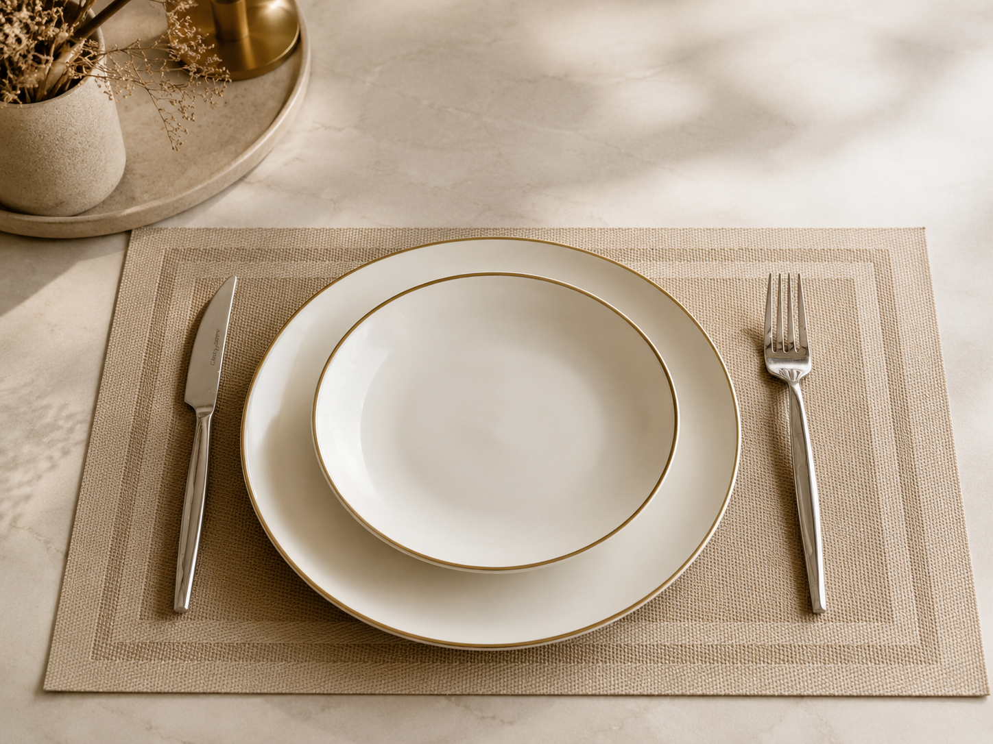Square light brown placemat with white gold-rimmed plates on dark dining table